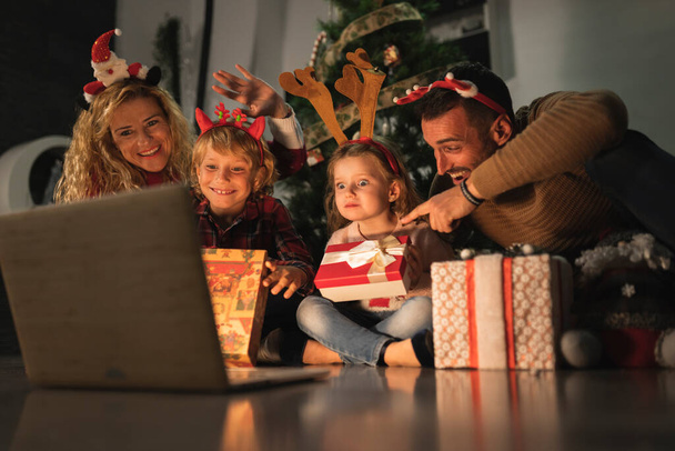 興奮した家族の4ビデオ通話前に開くクリスマスプレゼントで夜 - 写真・画像