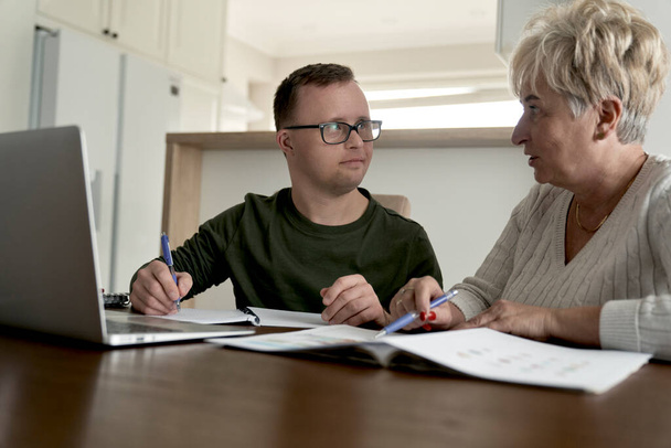 Biały mężczyzna z zespołem Downa uczy się z mamą w domu  - Zdjęcie, obraz