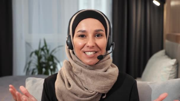 Мусульманська арабська ісламська дівчина, одягнена в хіджаб в навушниках, має онлайн відеодзвінок, посміхається вчительці фрілансу, яка консультується в Інтернеті, спілкується з віддаленими віртуальними розмовами в приміщенні - Кадри, відео