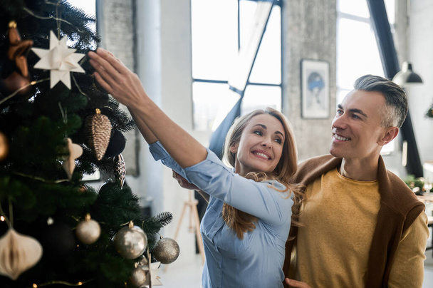 Weihnachten. Lächelndes Paar schmückt Weihnachtsbaum und sieht fröhlich aus - Foto, Bild