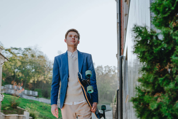 Smiling handsome young man businessman wearing suit messaging holding longboard walking street - Fotografie, Obrázek