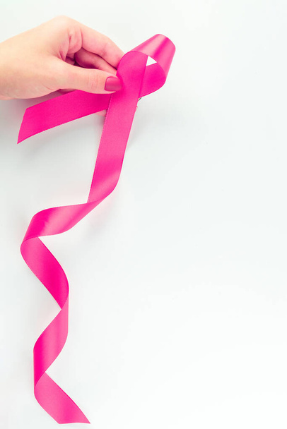 Dia do cancro. Fita rosa símbolo de cuidados de saúde em mãos de mulher no fundo branco. Conceito de suporte de câncer de mama com espaço de cópia - Foto, Imagem