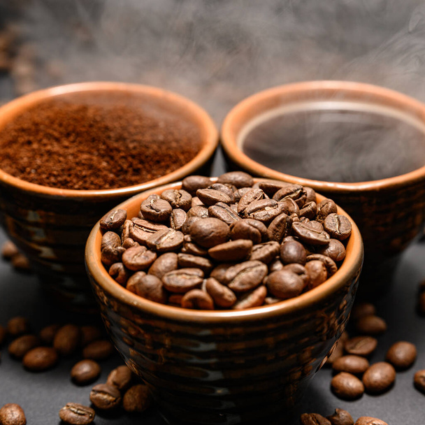 Vers gemalen en gebrouwen zwarte koffie op een zwarte achtergrond, drie kopjes met gestoomde koffie. - Foto, afbeelding