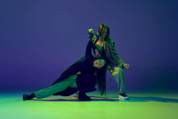 Emotions in motion. Two dancers, stylish fashionable dance couple dancing contemporary dance on colorful gradient blue-green background in neon light. Concept of art, creativity, movement, fashion - Photo, image