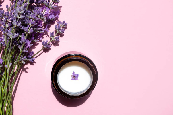 Biologische moisturizer en natuurlijk lavendel boeket in een glazen pot op een roze achtergrond. Vlakke lay, plaats voor tekst. - Foto, afbeelding