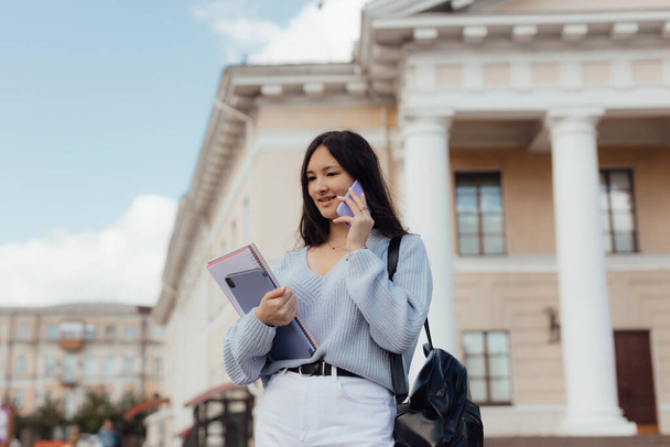 Girl student with notebooks and a tablet on the background of the university. Distance learning concept. Modern millennial youth lifestyle and travel concept. - Foto, imagen