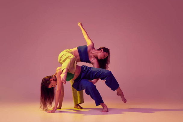 Contemporary dance couple in motion and action isolated on crystal pink background. Young stylish fashionable girls dancing. Concept of modern art, fashion, youth style and creativity - Zdjęcie, obraz