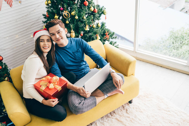 Молодая счастливая азиатская пара, сидящая вместе видео-звонок на ноутбуке с друзьями или родителями спасибо за подарок, полученный во время рождественских каникул. Празднуйте день бокса. - Фото, изображение