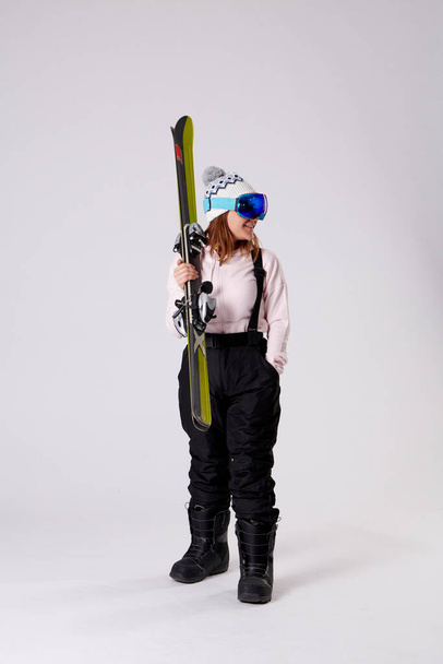 junge Frau mit Snowboardbrille, Skier mit einer Hand in der Hand und Blick zur Seite auf weißem Hintergrund. - Foto, Bild