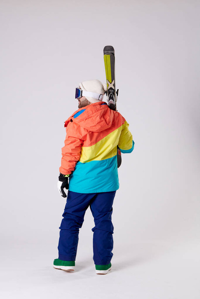 fiú hátulról snowboard ruhák kezében néhány síléc, miközben keresi a bal oldalon egy fehér háttér. - Fotó, kép