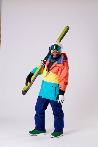 man in snowboard bril en snowgear houden ski 's in een hand, terwijl het kijken naar de camera op een witte achtergrond. - Foto, afbeelding