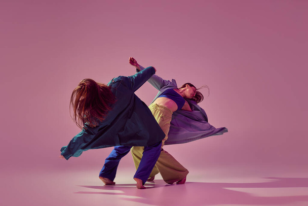 Contemporary dance couple in motion and action isolated on crystal pink background. Young stylish fashionable girls dancing. Concept of modern art, fashion, youth style and creativity - Photo, Image