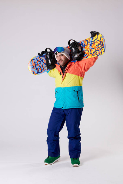 Man in snow gear holding a snowboard on his back and looking at the camera on a white background. - Foto, immagini