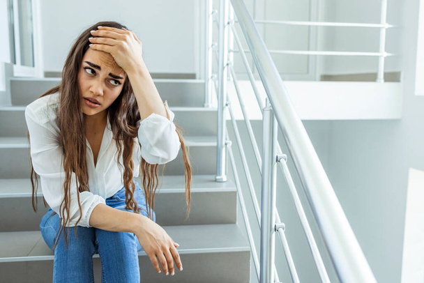 Depressed sad woman sitting on the stairs of a business building, businesswoman in business clothes tired. Business woman stressed from work while sitting indoors on the stairs - 写真・画像
