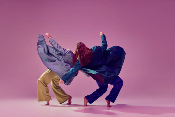 Современная танцевальная пара в движении и действие изолированы на кристально розовом фоне. Молодые модные девушки танцуют. Концепция современного искусства, моды, молодежного стиля и творчества - Фото, изображение