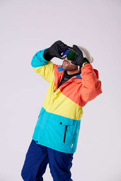 Kar içindeki çocuk iki eliyle snowboard gözlüğü takıyor ve beyaz bir arka plana bakıyor.. - Fotoğraf, Görsel