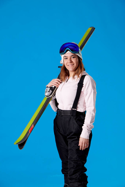 Smiling girl ready for the snow, looking at the camera and holding skis on a blue background. - Foto, Imagem