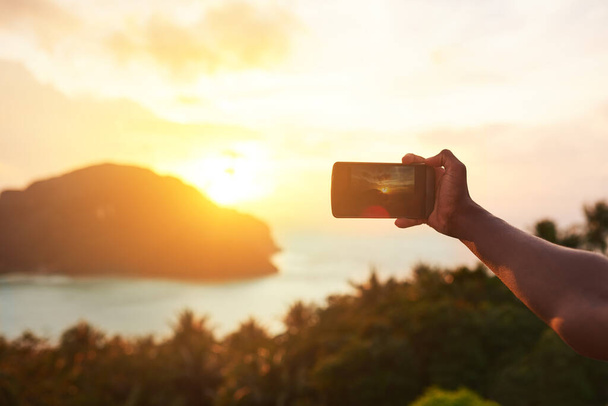 Every sunset is a poem without words. an unidentifiable tourist using a smartphone to photograph an island view - Фото, изображение