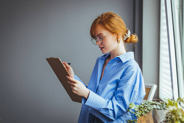 beautiful red-haired girl holding clipboard making notes - 写真・画像