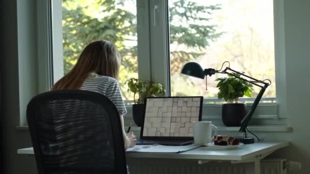 Thuis kantoor werkplek met laptop. Een vrouw die thuis werkt met een laptop. Vrouwelijke freelancer zit aan tafel bij het raam - Video