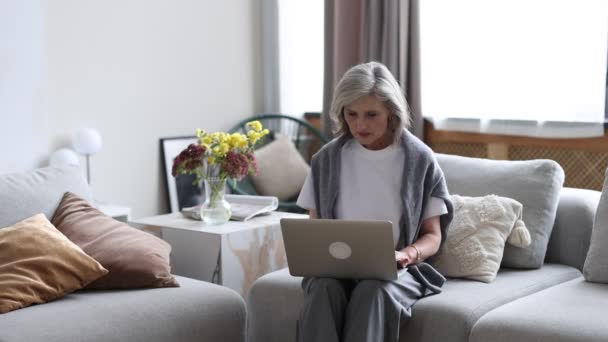 жінка працює на ноутбуці вдома, сидячи на дивані. - Кадри, відео