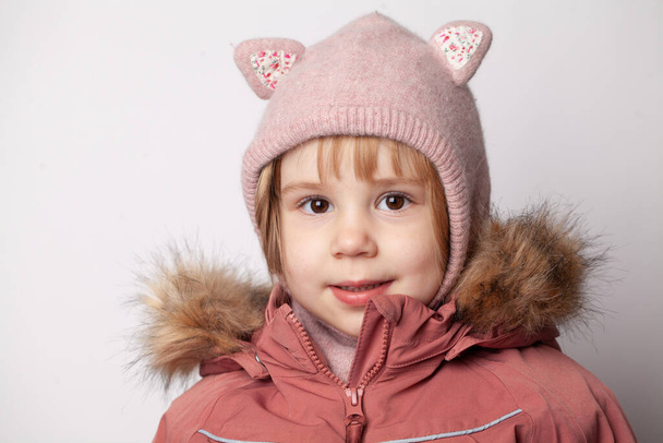 Portré aranyos kislány rózsaszín kabát és kalap fehér stúdió fal háttér - Fotó, kép