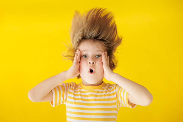 Surprised child holding face. Shocked kid against yellow background. Boy wearing striped shirt. Summer vacation and travel concept - Foto, immagini
