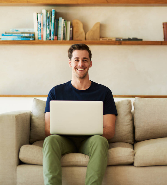 Tutustu blogiini. Muotokuva komea nuori mies käyttää hänen laptop istuessaan sohvalla kotona - Valokuva, kuva