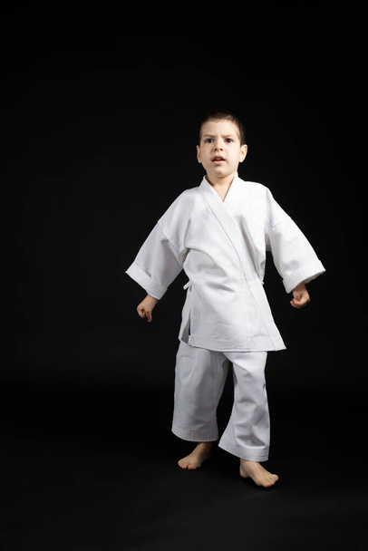Mały chłopiec w kimono ćwiczy karate na czarnym tle. Sztuki walki dla dzieci. - Zdjęcie, obraz