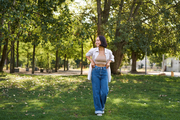 Heureuse fille asiatique marchant dans le parc, sentant la liberté et la joie, marchant à l'extérieur le jour ensoleillé. - Photo, image