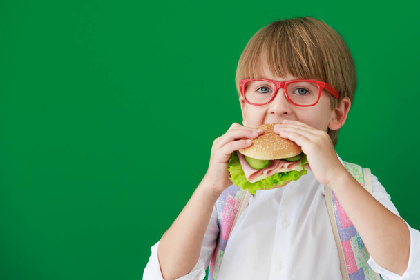 Funny child student with hamburger in class. Happy kid against green chalkboard. Education and back to school concept - Valokuva, kuva