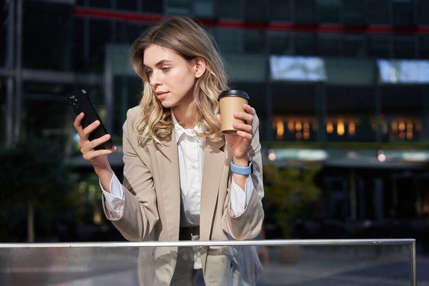 Bedrijfsmensen. Jonge zakenvrouw drinken van koffie, met behulp van smartphone app, rusten op lunchpauze. - Foto, afbeelding