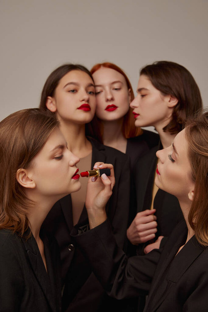 Retrato de mulheres bonitas jovens em jaquetas pretas e batom vermelho, aplicando maquiagem, posando sobre fundo cinza. Conceito de beleza, liberdade, emoções, moda extraordinária, estilo moderno, juventude - Foto, Imagem