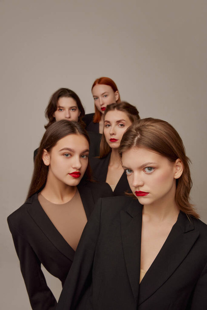 Portré fiatal gyönyörű nők fekete kabát és piros rúzs smink pózol szürke háttér. A modellek nézik. Fogalom szépség, szabadság, érzelmek, rendkívüli divat, modern stílus, fiatalok - Fotó, kép