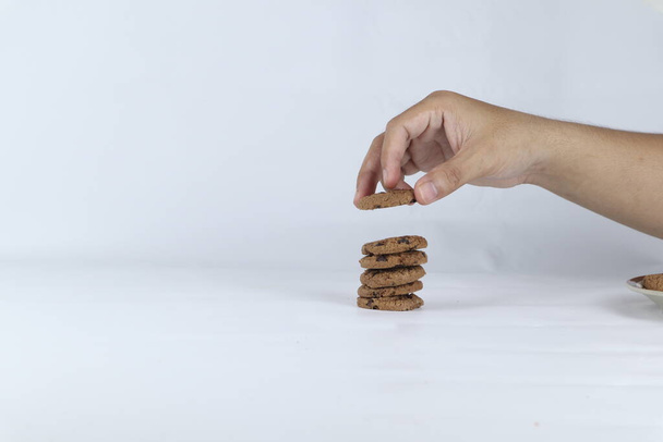 mains empilant des biscuits sur un fond blanc. Main humaine prenant cookie d'avoine d'une pile - Photo, image