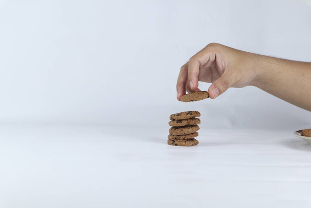 mains empilant des biscuits sur un fond blanc. Main humaine prenant cookie d'avoine d'une pile - Photo, image