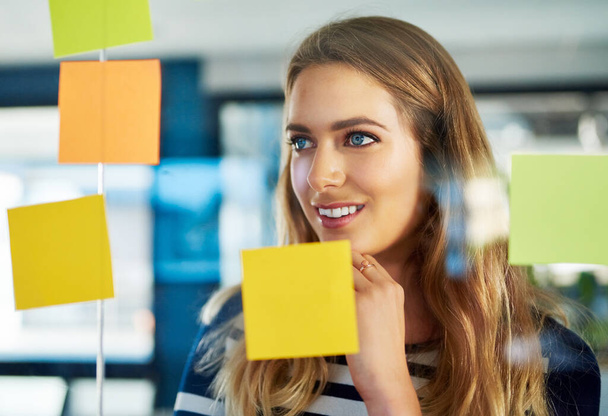 Stimulating creativity with a brainstorming session. a young woman having a brainstorming session with sticky notes at work - Photo, image