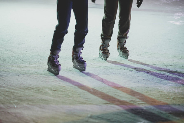Schlittschuhläufer auf der Eisbahn, Schlittschuhe aus nächster Nähe. Leute, die sich abends auf dem Stadtplatz amüsieren und Schlittschuh laufen. Beine mit Schlittschuhen schnitten die Sicht ab. Stimmungsvoller Winterurlaub in Europa. Frohe Feiertage! - Foto, Bild