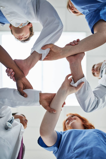 Salvar vidas es un esfuerzo de equipo. Inyección de bajo ángulo de un grupo de médicos que unen sus manos en unidad - Foto, imagen