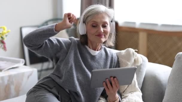 Доглянута Сильна жінка в навушниках вдома Сидячи на дивані слухати музику і дивитися відео на планшеті. - Кадри, відео