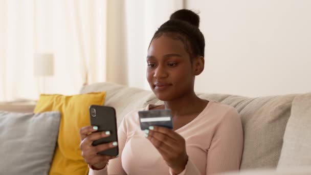 Pagamento online di successo. Giovane donna afroamericana che paga via internet, utilizzando l'app bancaria su smartphone e carta di credito a casa, tracking shot, rallentatore, spazio libero - Filmati, video