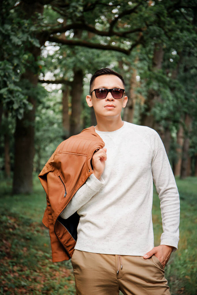 Happy young handsome man in a leather jacket and sunglasses outdoors - Fotografie, Obrázek