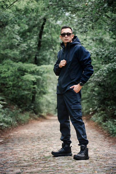 Ένας κτηνώδης άντρας με μαύρα ρούχα περπατάει στο δρομάκι στο ομιχλώδες δάσος. - Φωτογραφία, εικόνα