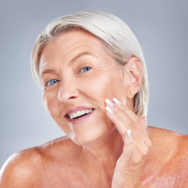 Skincare, wellness and senior woman with face for inspection, health and beauty against a grey studio background. Happy, smile and portrait of an elderly person with facial care during retirement. - Photo, Image