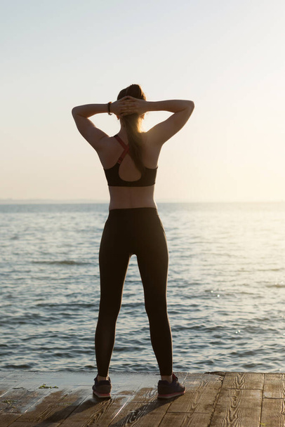 girl athlete, faces the sea, looks at the dawn, goes in for sports, concept, lifestyle - Photo, Image