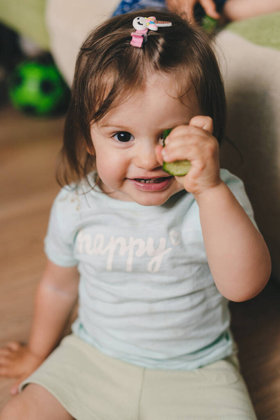 Egy mosolygó lány portréja, aki uborkát tart a kamerában. Mosolygó boldog gyermek. Boldog család, gyermekkor. - Fotó, kép
