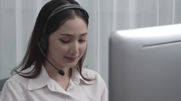 Aasian asiakastuki operaattori yllään kuulokkeet ja mikrofoni työskentelee hänen työpöytä kannettavan tietokoneen. Innostunut naispuolinen työntekijä tarjoaa asiakaspalvelua, tukeva Call Center agentti auttaa asiakkaita. - Materiaali, video