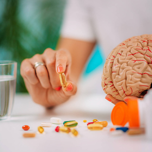 Cognitive improvement or brain supplements. Woman holding a supplement capsule and a model brain. - Foto, Bild