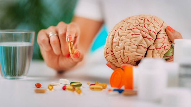 Cognitive improvement or brain supplements. Woman holding a supplement capsule and a model brain. - Φωτογραφία, εικόνα