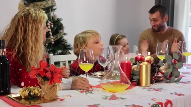 Blanke familie van vier met kerstmutsen die het kerstdiner vieren. Focus op kaars - Video